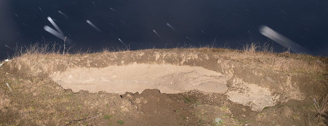 das Bild zeigt einen Erdkrater und darüber einen dunkelblauen Nachthimmel mit "Sternschnuppen"