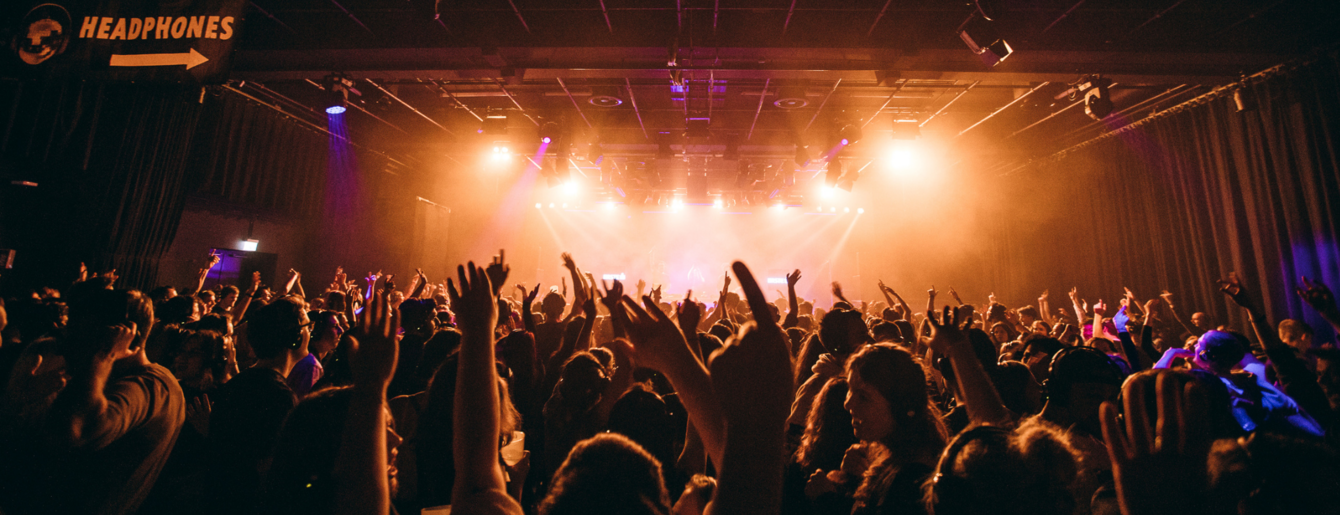 Große Menschenmenge bei einer Silent Disco mit erhobenen Händen vor einer hell beleuchteten Bühne
