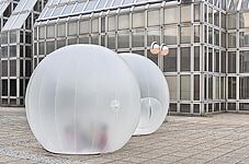 Zwei durchsichtige, aufblasbare Kugeln auf einem gepflasterten Platz vor einem modernen Glasgebäude