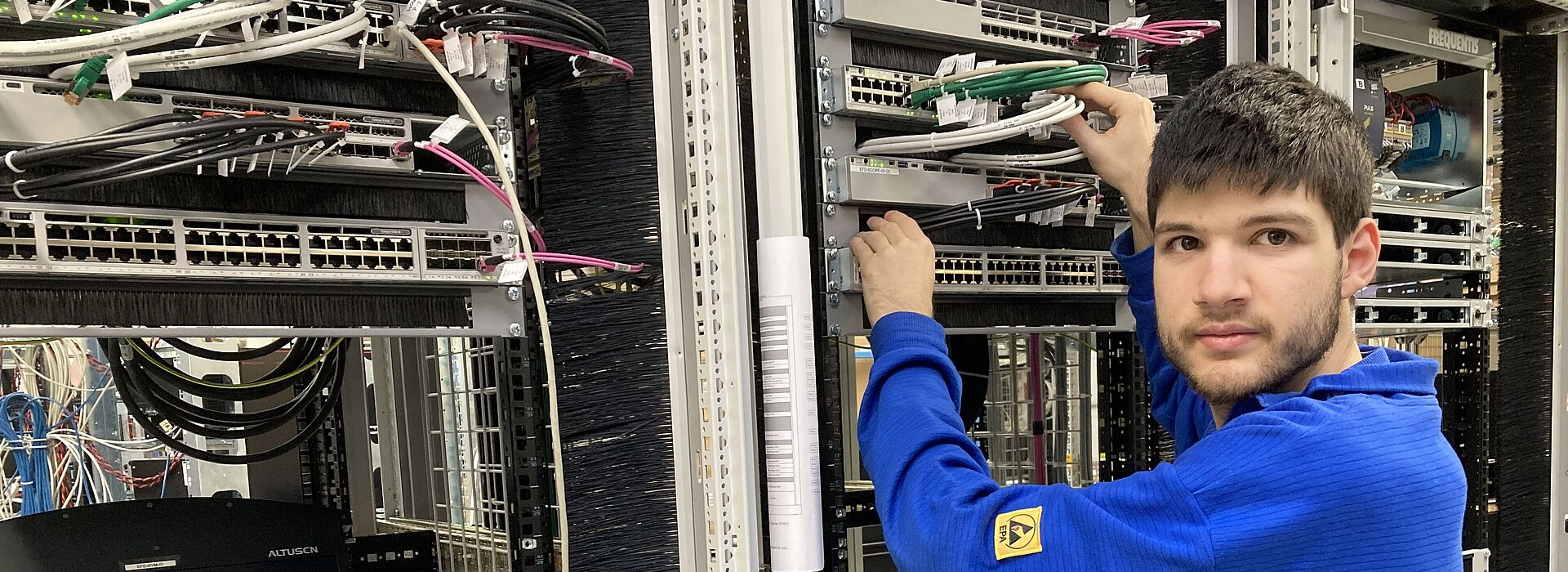 Person in blauem Pullover arbeitet an einem Serverrack mit Netzwerkkabeln in einem Rechenzentrum.