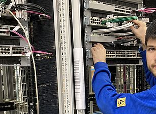 Person in blauem Pullover arbeitet an einem Serverrack mit Netzwerkkabeln in einem Rechenzentrum.