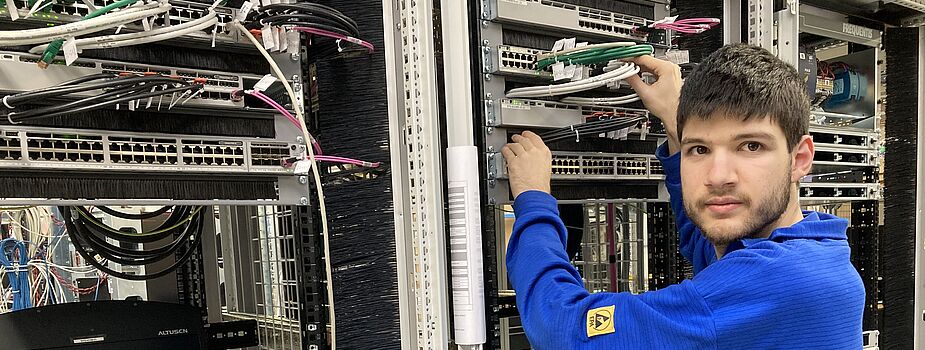Person in blauem Pullover arbeitet an einem Serverrack mit Netzwerkkabeln in einem Rechenzentrum.