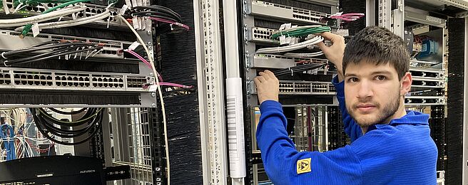 Person in blauem Pullover arbeitet an einem Serverrack mit Netzwerkkabeln in einem Rechenzentrum.