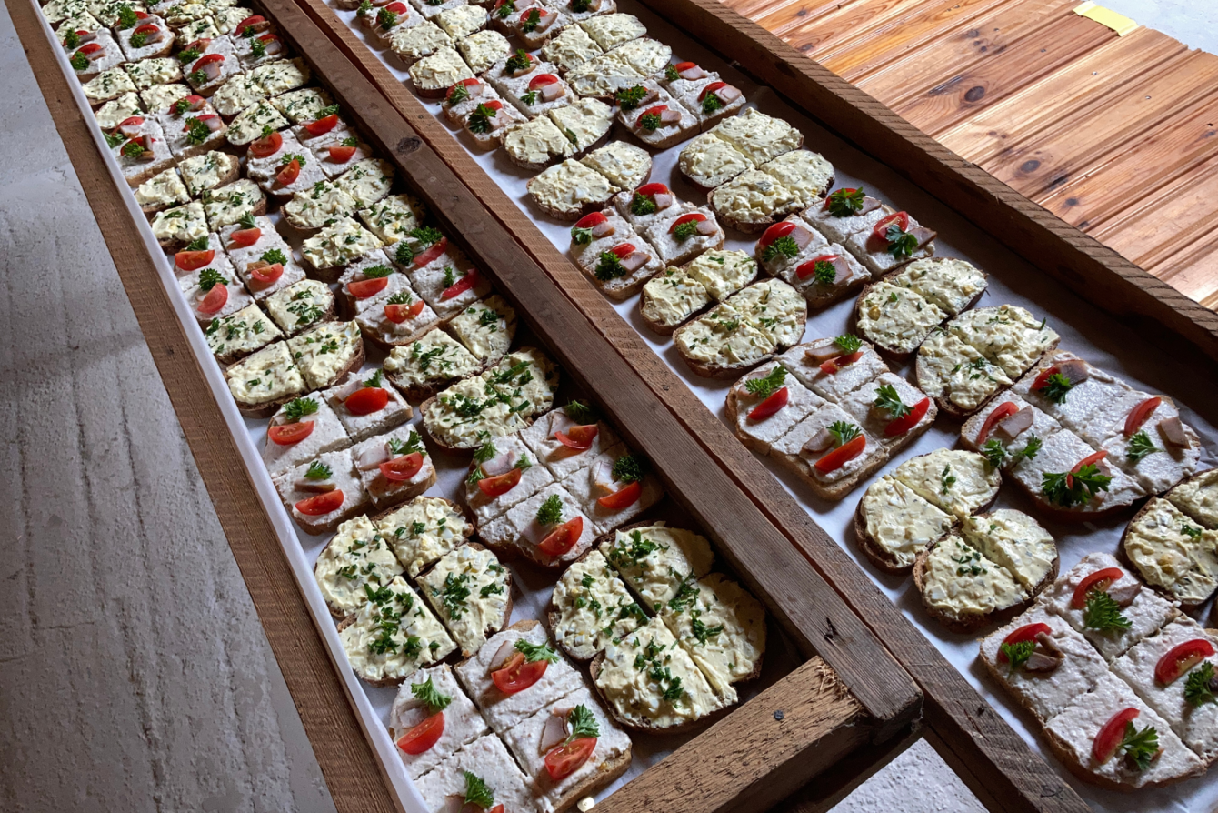 Viele belegte Brotscheiben mit Frischkäse, Tomatenscheiben und Kräutern auf Holztabletts angerichtet