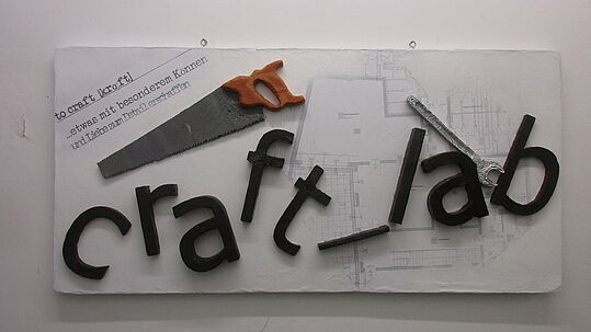 Ein Schild mit dem Schriftzug "craft_lab" mit einer Säge auf einem Raumplan
