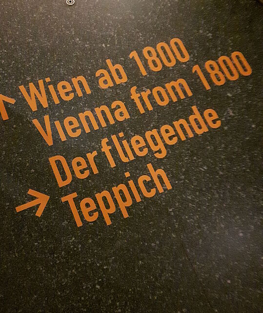 Die Aufschrift "Der fliegende Teppich" mit Pfeil am Boden im Wien Museum