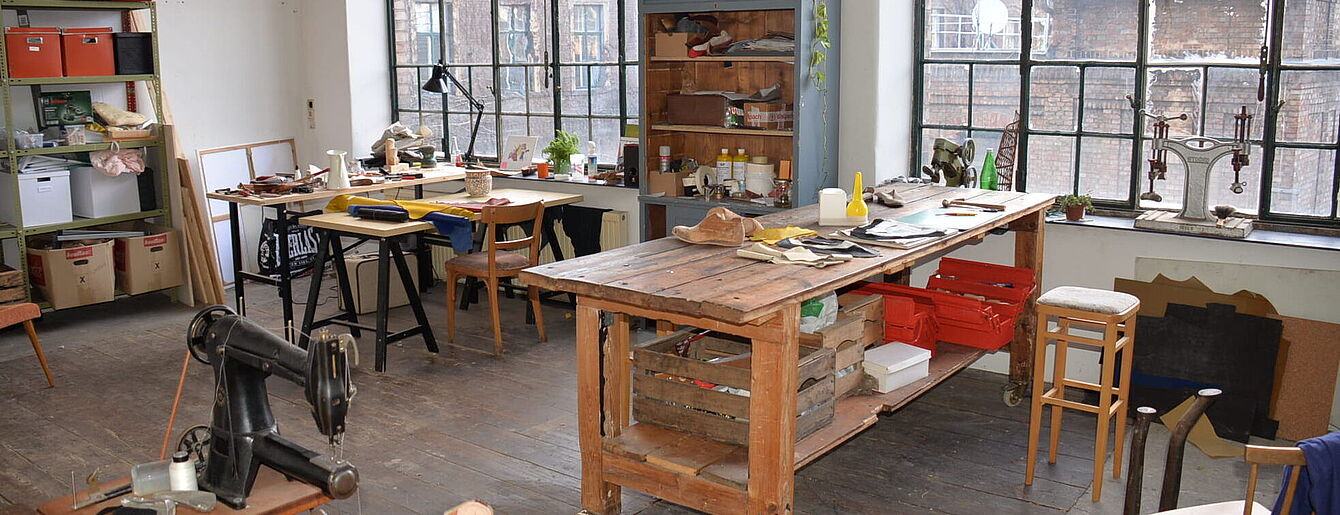 Werkstatt mit großen Fenstern, Holztischen, Lederwerkzeugen und Nähmaschine für Leder und Design