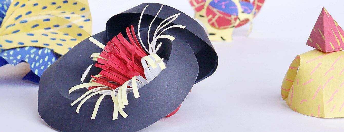 Mehrere bunte Papierskulpturen mit unterschiedlichen Formen und Mustern auf weißem Hintergrund