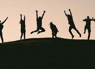 Photo by Val Vesa on Unsplash Silhouetten mehrerer Menschen, die auf einem Hügel springen und Arme heben