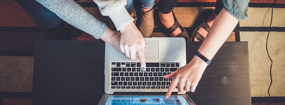 Zwei Personen zeigen auf den Bildschirm eines Laptops auf einem Tisch, um Bildungsberatung im Kompetenzpool zu unterstützen