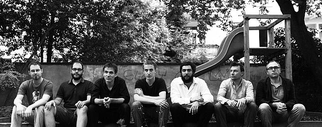 Schwarz-weiß-Foto von Musikern der JazzWerkstatt nebeneinander sitzend vor einer Rutsche