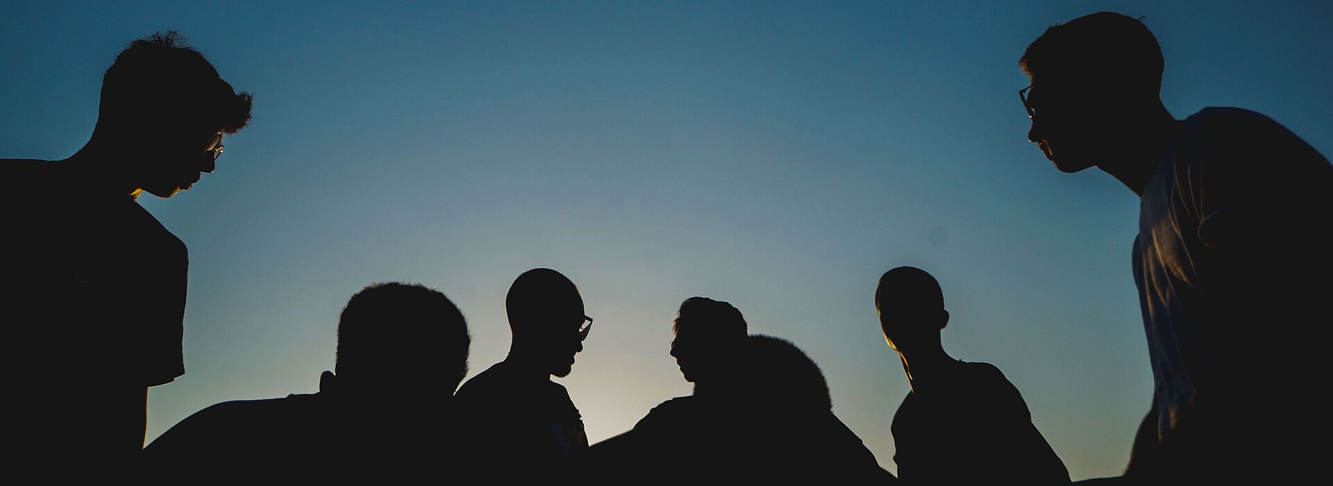 Silhouetten von 6 jungen Burschen vor blauem Himmel