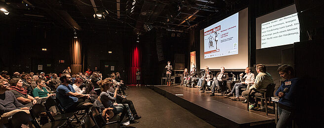 Publikum und Teilnehmer_innen der Podiumsdiskussion