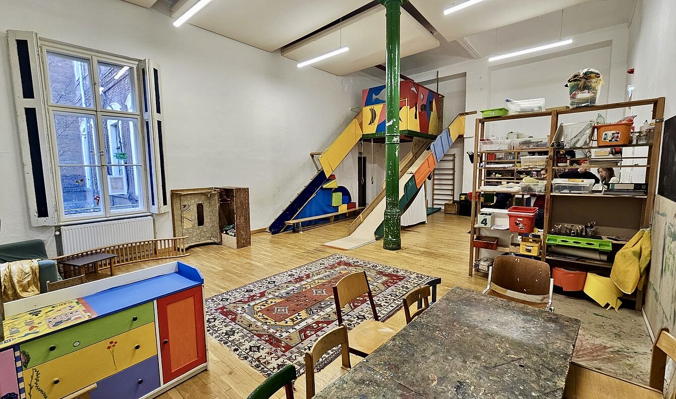 Kinderspielzimmer mit Rutsche, buntem Spielmöbel, Teppich und Regalen mit Spielzeug und Bastelmaterialien