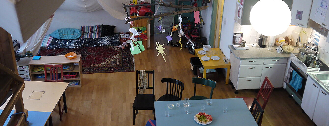 Kinderinsel im WUK mit Esstisch, Stühlen, Spielbereich mit Teppichen und Kissen sowie Küchenzeile