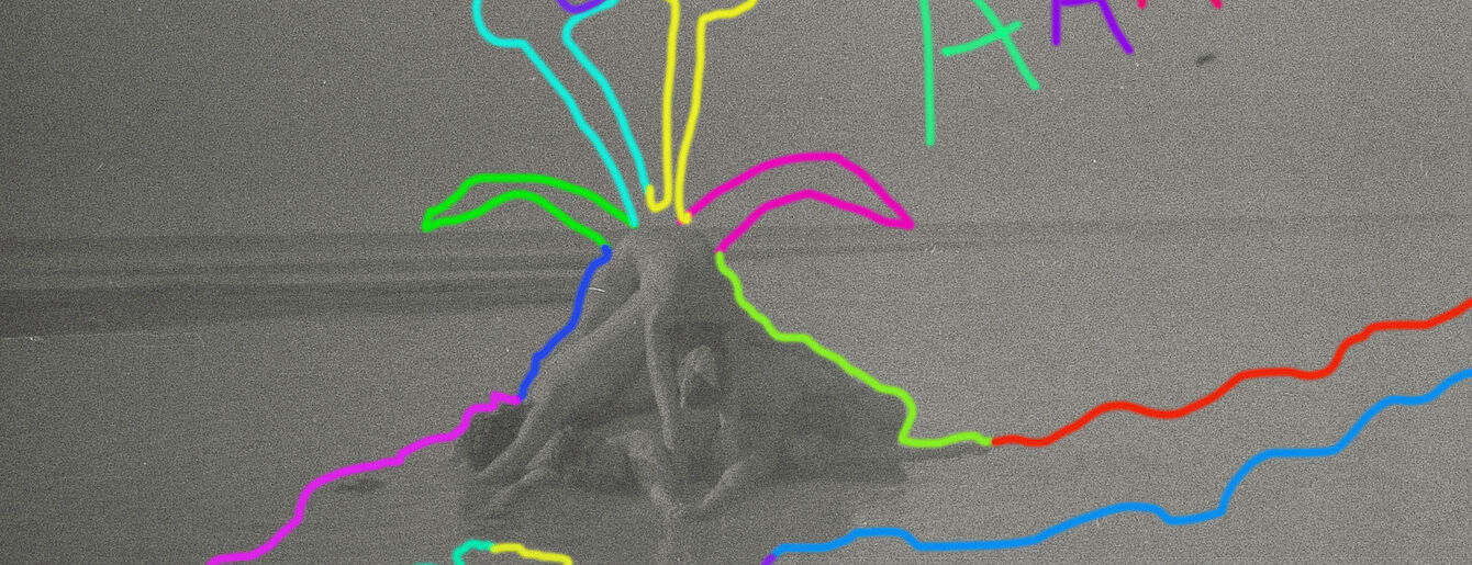 Außenaufnahme eines Graustufenbildes, wahrscheinlich ein altes Foto oder eine Filmsequenz. Im Vordergrund ist ein Strand oder eine Sandfläche zu sehen. Mehrere undeutliche menschliche Figuren sind umeinander gruppiert, liegen oder sind so positioniert, dass sie eine Art von Aktivität vermuten lassen. Den Figuren fehlen klare Details, sie erscheinen als helle oder dunkle Formen vor dem umgebenden Sand oder Wasser. Die Szene ist etwas unscharf oder körnig mit einer spürbaren Textur, die typisch für ältere Fotografien oder Filmabzüge ist. Der gesamte Tonwertumfang ist gedämpft und besteht hauptsächlich aus Grautönen mit subtilen Schattierungen. Es ist keine deutliche Färbung vorhanden. Der Hintergrund ist ein ähnlicher gedämpfter Grauton, der sich über das Bild hinaus erstreckt, und es fehlt jegliches kontrastierende Licht oder Schatten, das die Figuren besonders auffällig machen würde.