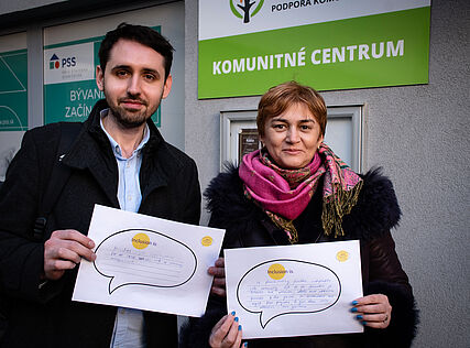 Zwei Menschen mit Papieren mit der Aufschrift "Inclusion is" vor dem Komunitné Centrum in Bratislava