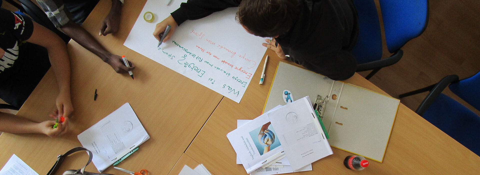Tisch mit Zetteln, Stiften und Flipchart-Blatt und Menschen von oben