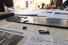 Nahaufnahme eines mit Wassertröpfchen bedeckten Metallstreifens auf einer Zeitung mit Text und einem Foto im Hintergrund