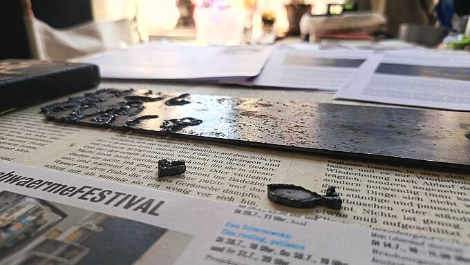 Nahaufnahme eines mit Wassertröpfchen bedeckten Metallstreifens auf einer Zeitung mit Text und einem Foto im Hintergrund