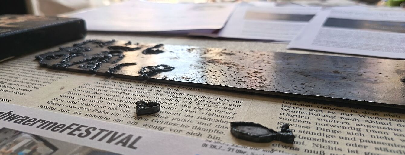 Nahaufnahme eines mit Wassertröpfchen bedeckten Metallstreifens auf einer Zeitung mit Text und einem Foto im Hintergrund.