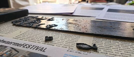 Nahaufnahme eines mit Wassertröpfchen bedeckten Metallstreifens auf einer Zeitung mit Text und einem Foto im Hintergrund