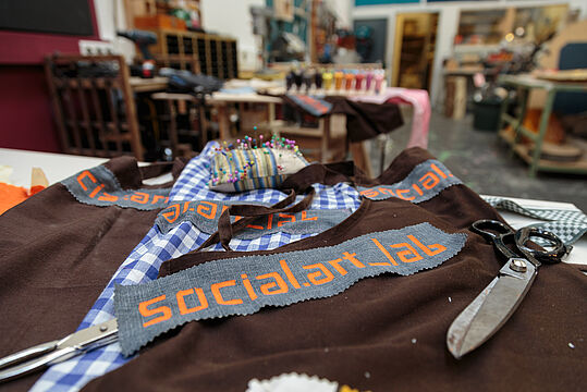 Textilien und ein mit "social.art_lab" bedruckter Stoffstreifen liegen am Tisch