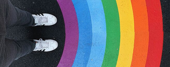 Füße einer Person vor einem auf den Boden gemalten Regenbogen