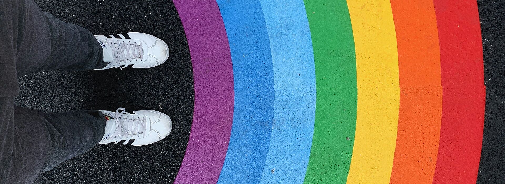 Füße einer Person vor einem auf den Boden gemalten Regenbogen