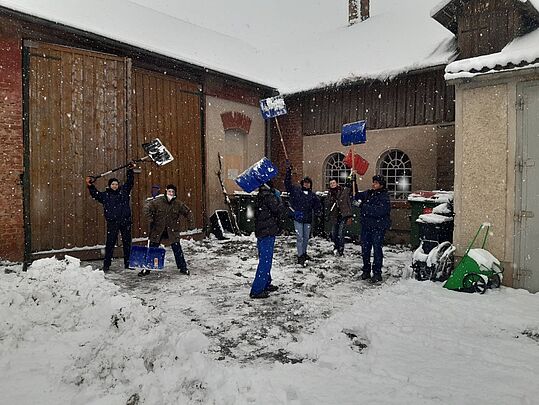 Gruppe von Menschen mit Schneeschaufeln in einem schneebedeckten Hof vor Gebäuden