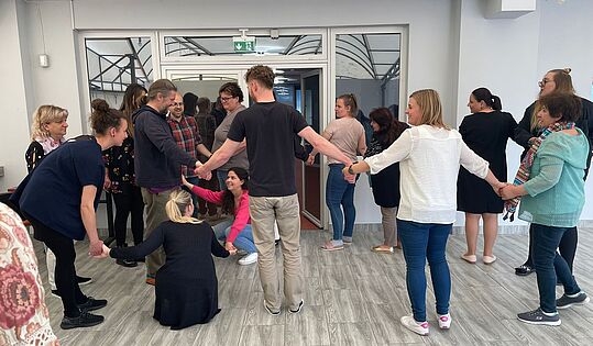 Teilnehmer_innen stehen in einem Kreis und halten die Hände