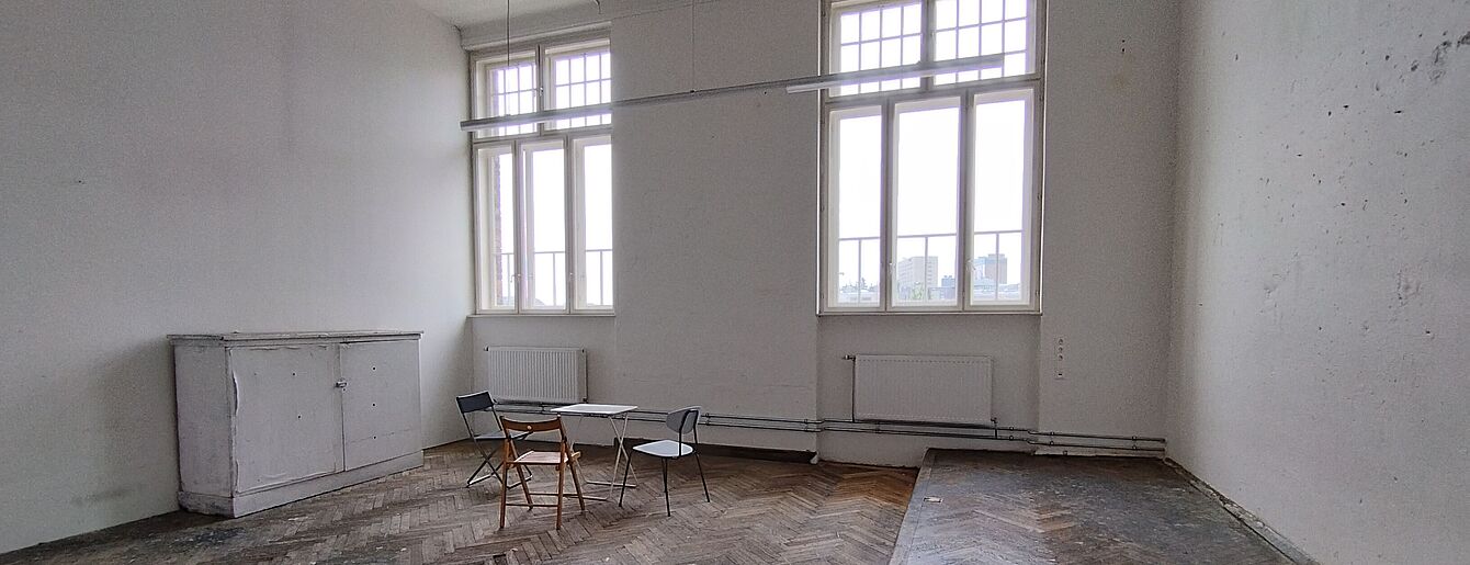 ein nahezu leerer, großer Raum mir hohen Fenstern