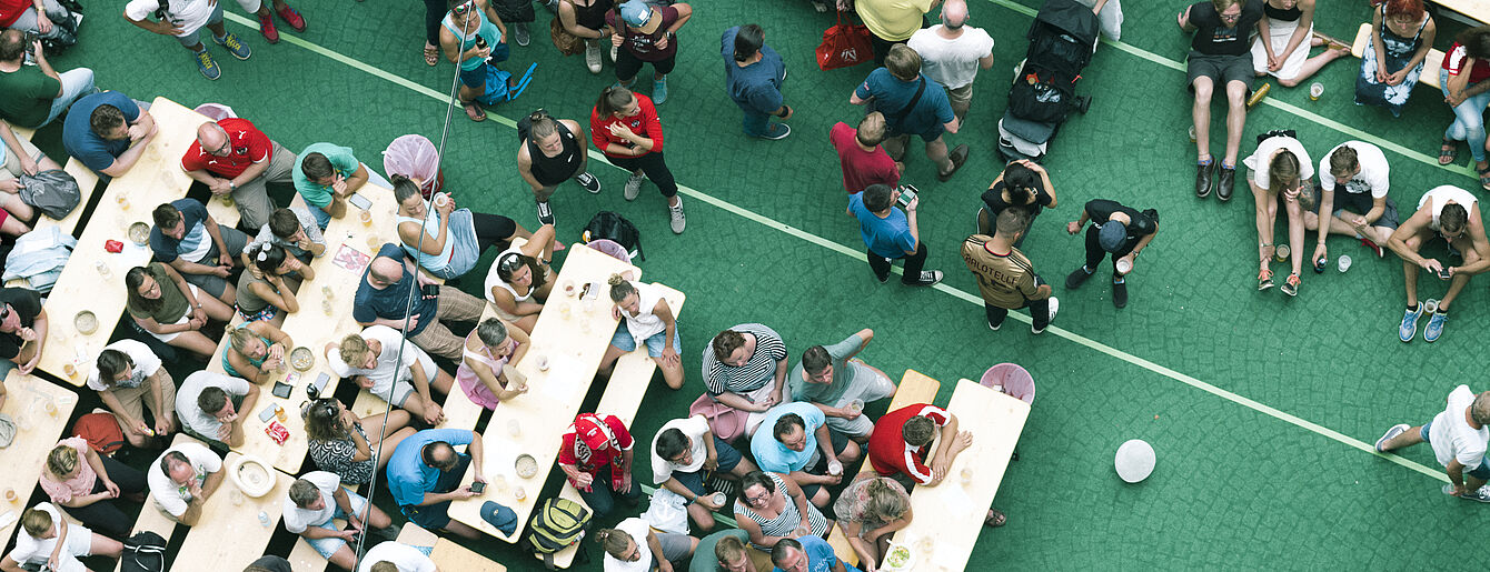 Women's Euro 2017 Public Viewing im WUK (c) Niko Ostermann Menschen sitzen an Holztischen und auf dem Boden auf grünem Bodenbelag bei einer Veranstaltung
