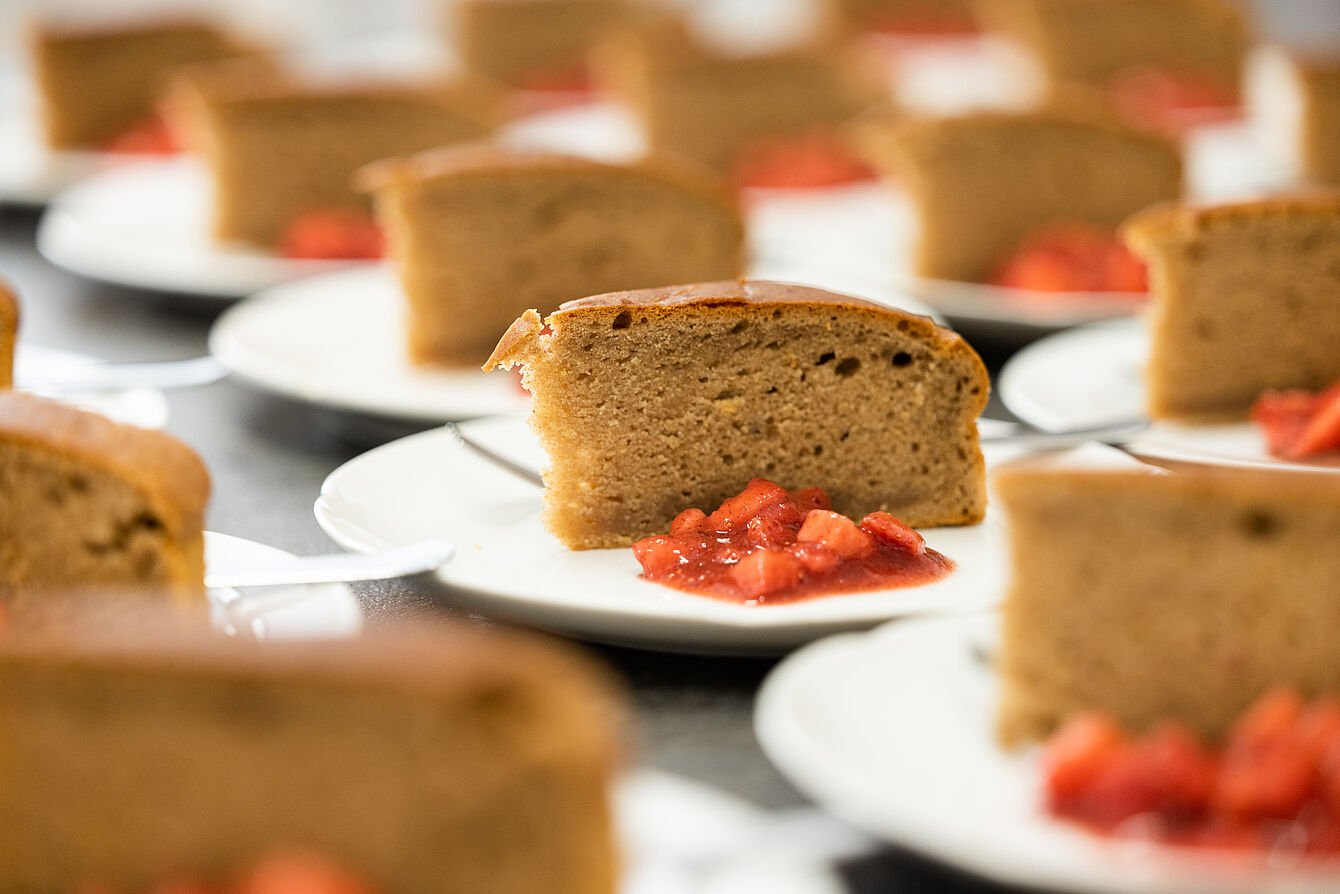 Mehrere Teller mit je einem Stück braunem Kuchen und einer Portion gewürfelter Erdbeeren