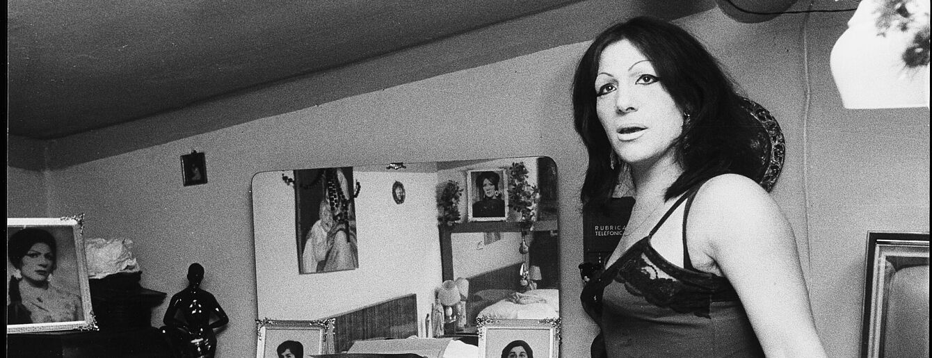 Ausschnitt aus eiber Schwarz-weiß Fotografie. Eine Frau schreitet durch das Zimmer und schaut dabei in die Kamera